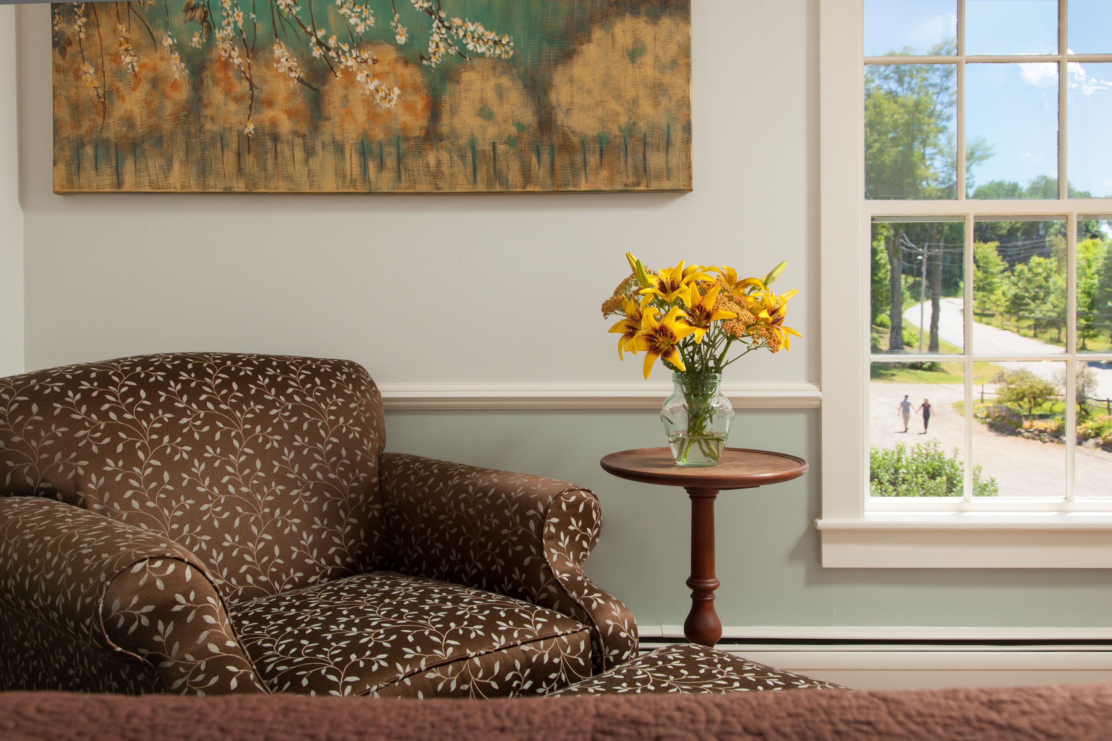 A room with a patterned sofa, a vase with yellow flowers, and a painting on the wall.