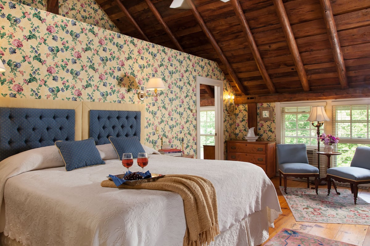 A bedroom with a large bed, floral wallpaper, and a wooden ceiling.