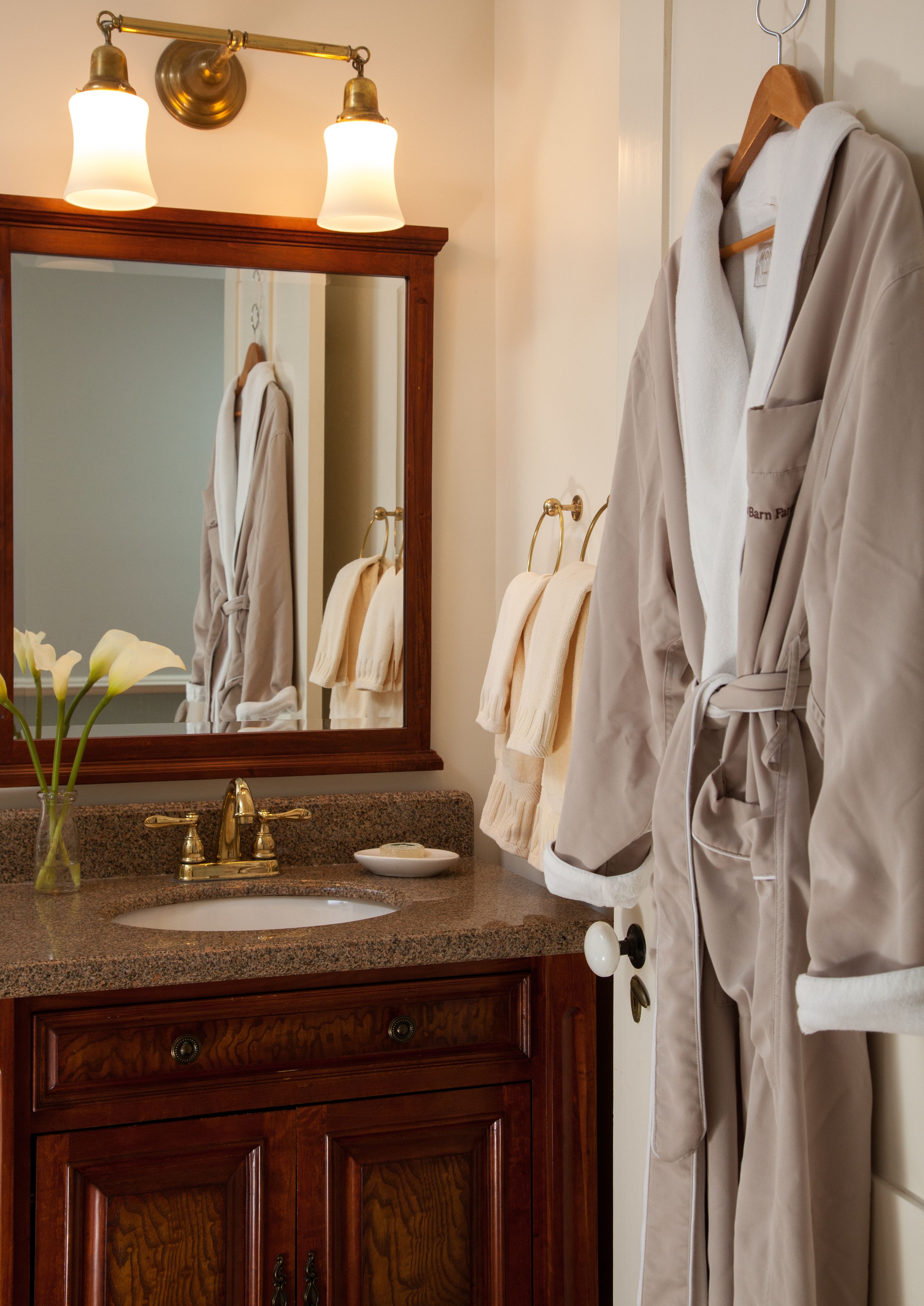 Une salle de bain avec un meuble-lavabo en bois, un grand miroir et un peignoir suspendu à un porte-manteau.