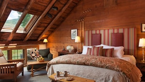 A cozy room with a wooden ceiling, a large bed with striped pillows, a small table with a basket and mugs, and a view of greenery through skylights. - The Inn at Round Barn Farm (Waitsfield)