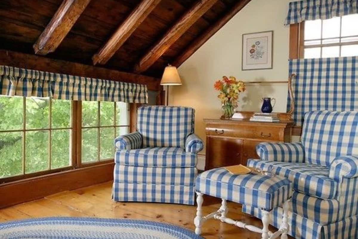 A room with checkered blue and white armchairs, a wooden desk, and a window with a view of greenery.