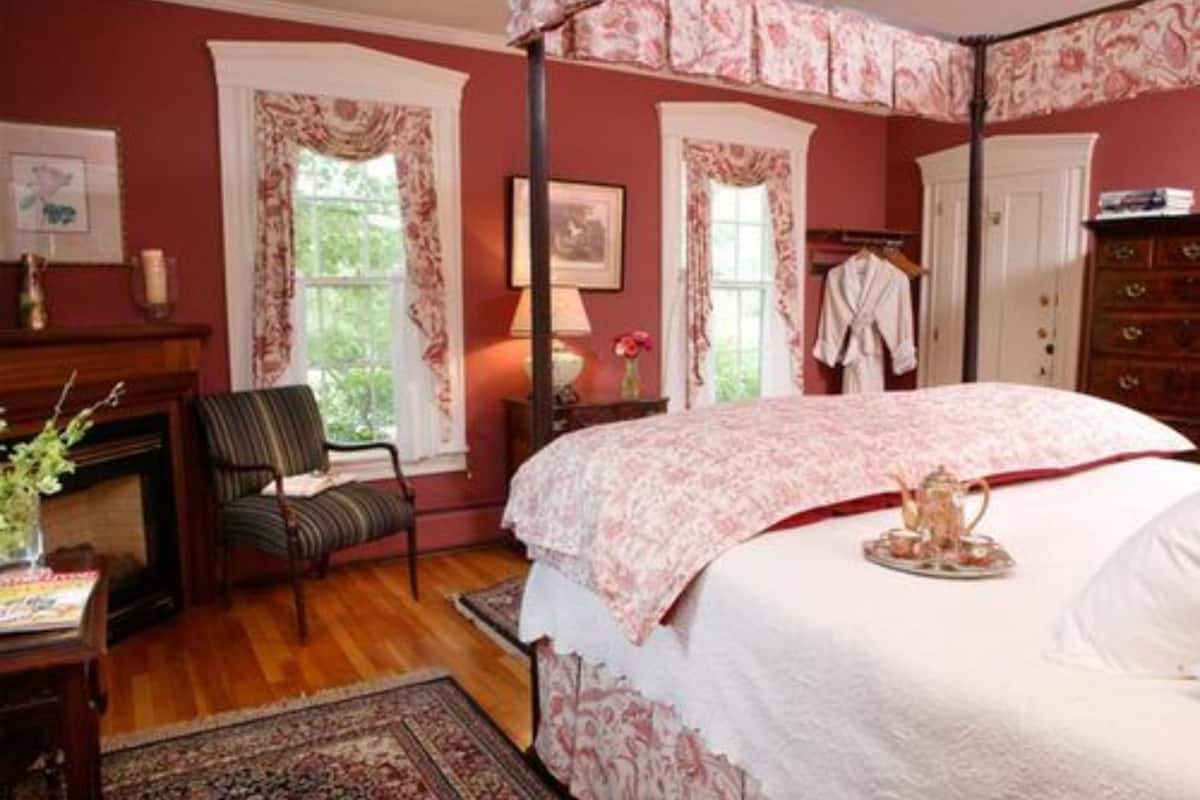 A bedroom with a four-poster bed, a fireplace, a chair, and a dresser.