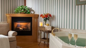 A cozy room with a fireplace, a comfortable armchair, a small table with a vase of flowers, and a bathtub with glasses of champagne. - The Inn at Round Barn Farm (Waitsfield)