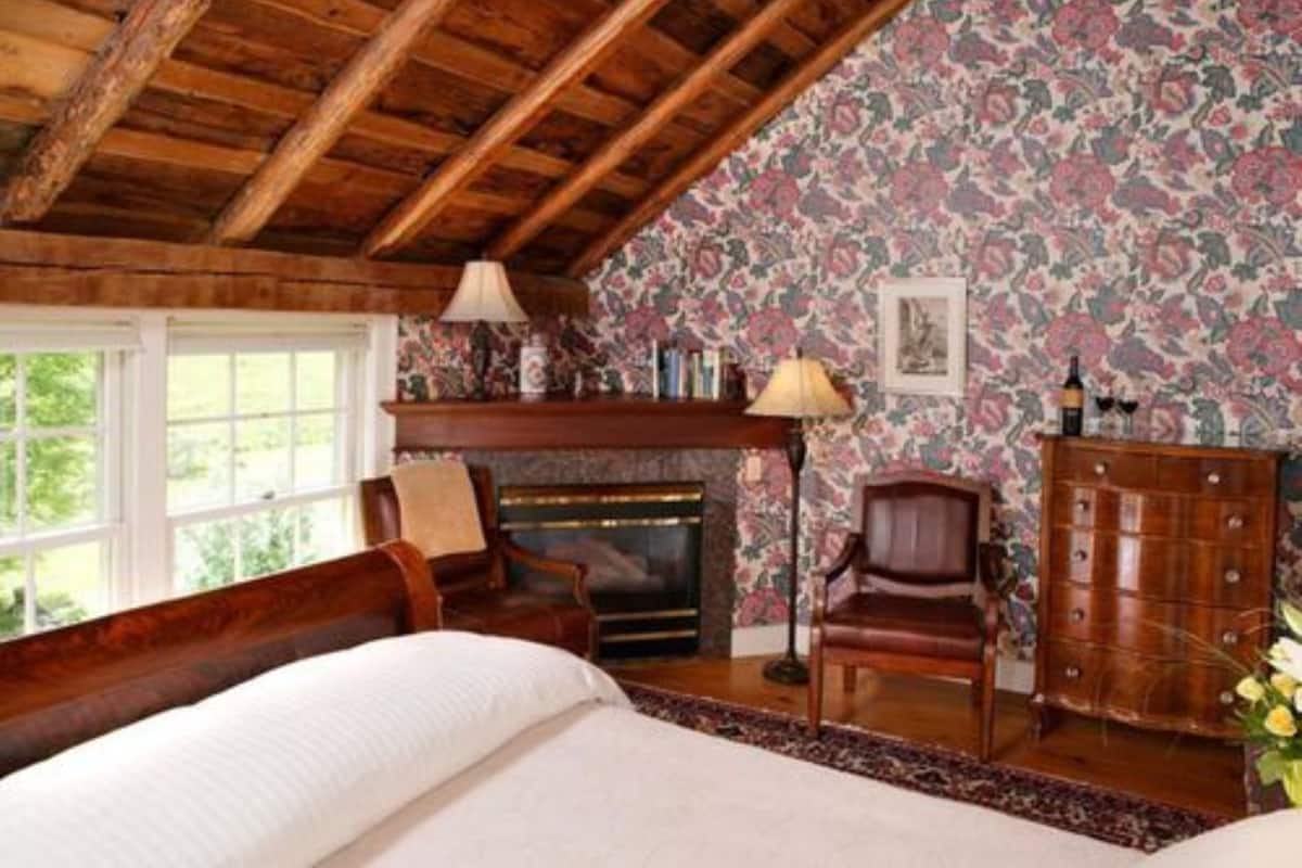 A cozy room with a wooden ceiling, a fireplace, a large bed, and floral wallpaper.