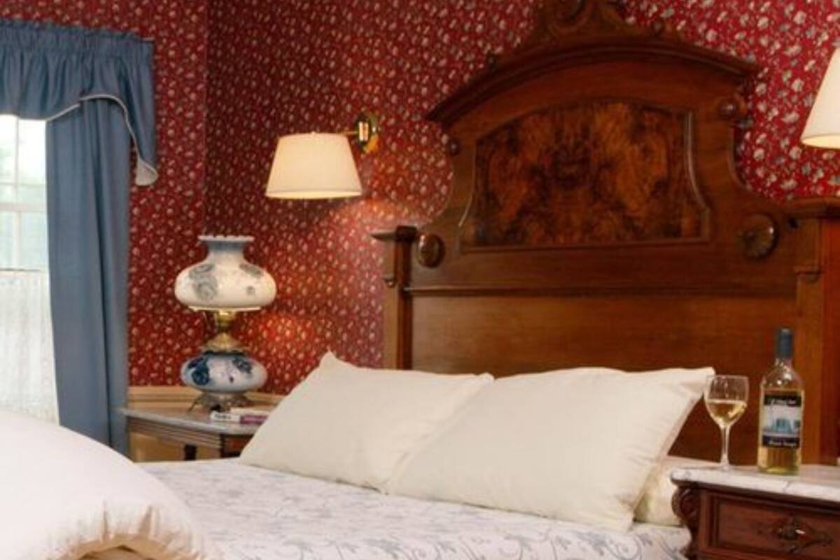 A hotel room with a wooden headboard, a bed with white linens, a bedside table with a lamp, and a bottle of wine on the nightstand.