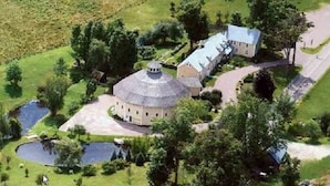 An aerial view of a property with a central circular building, a smaller adjacent structure, and a pond. - The Inn at Round Barn Farm (Waitsfield)