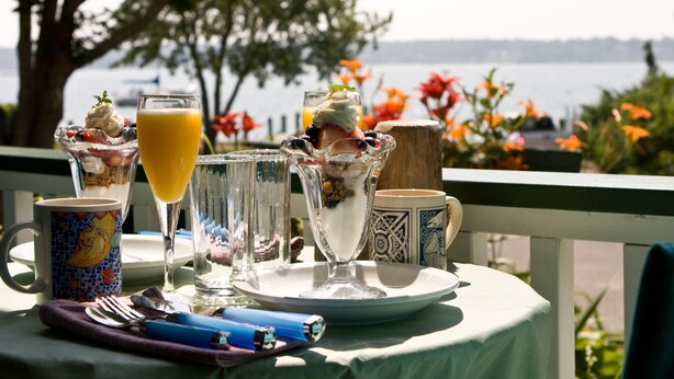 A table set with a glass of orange juice, a glass of white wine, and a dessert with whipped cream and berries.