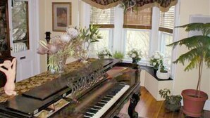 A grand piano in a room with a large window, a chandelier, and various plants.