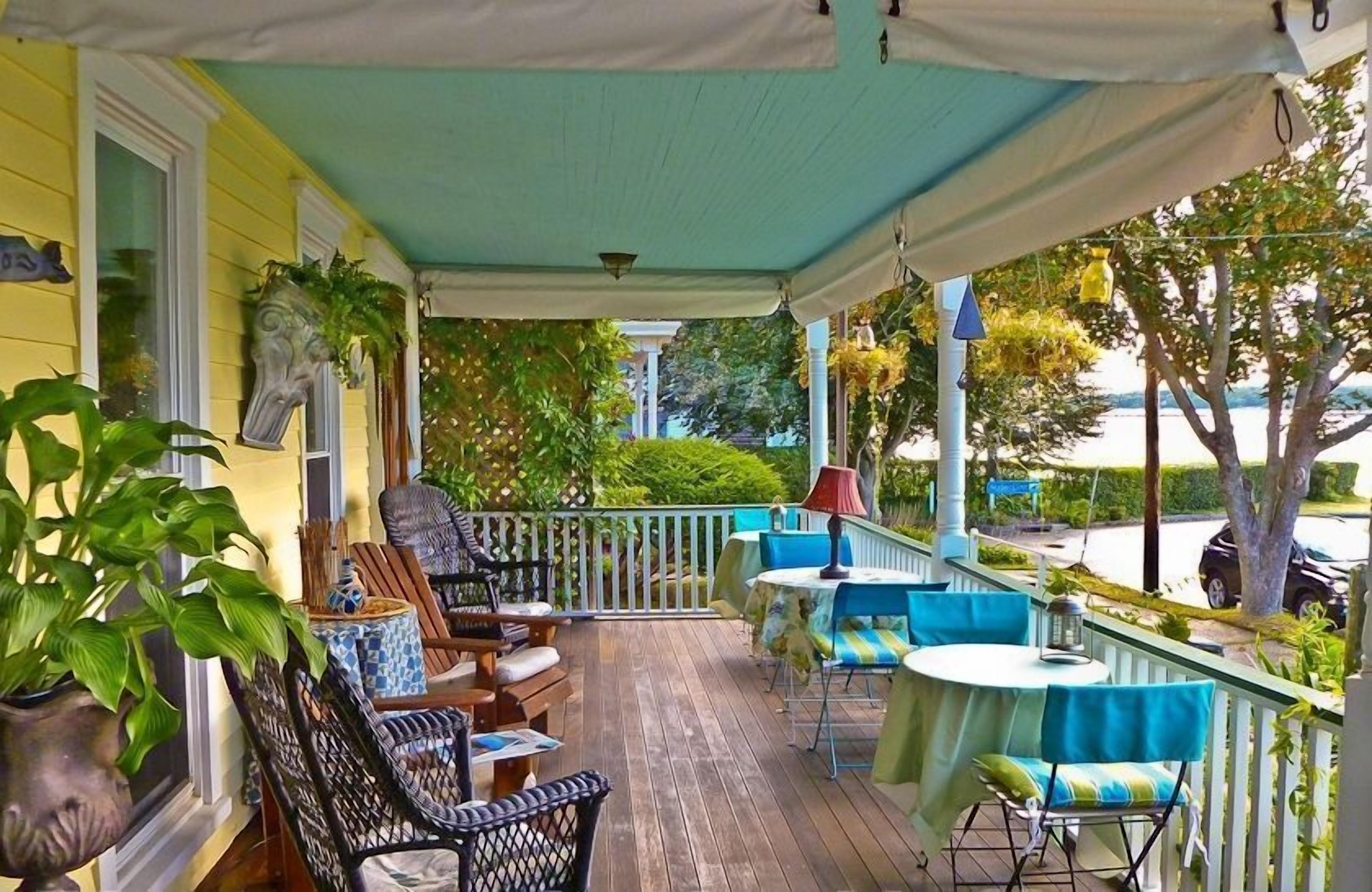 A covered porch with outdoor seating, including chairs and tables, and a view of the surrounding greenery.