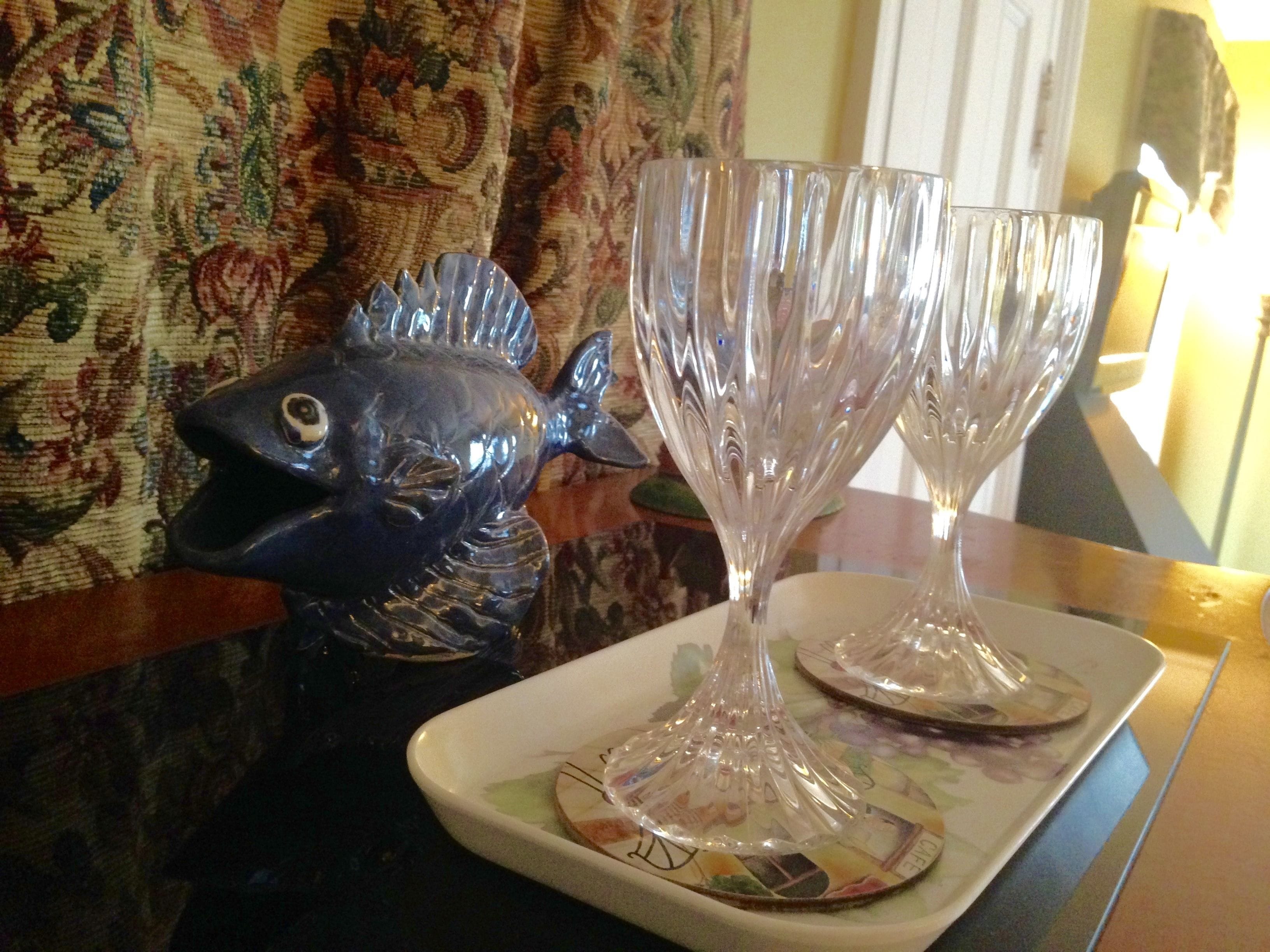 A decorative fish sculpture and two crystal glasses on a table with a patterned tablecloth.