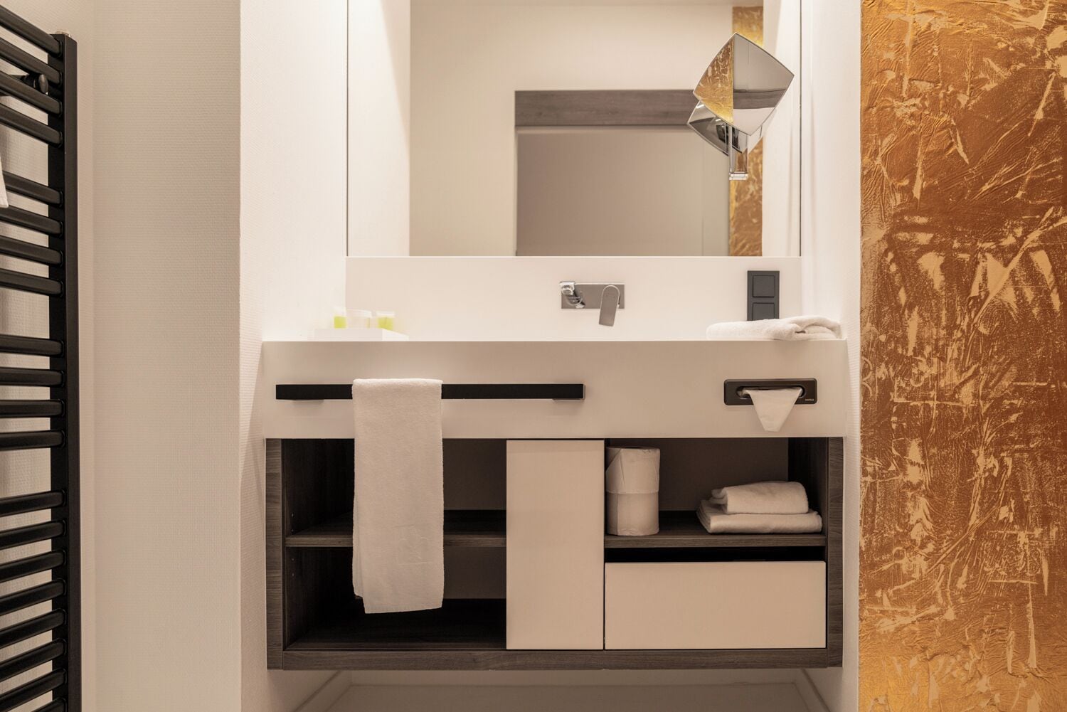 A modern bathroom with a built-in sink, mirror, towel rack, and storage cabinet.