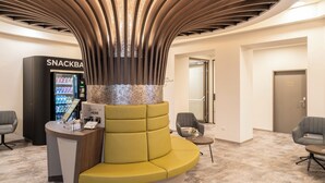 A modern lobby with a curved yellow seating area, a snack bar, and a check-in counter. - CHRIZZ Rooms (Graz)