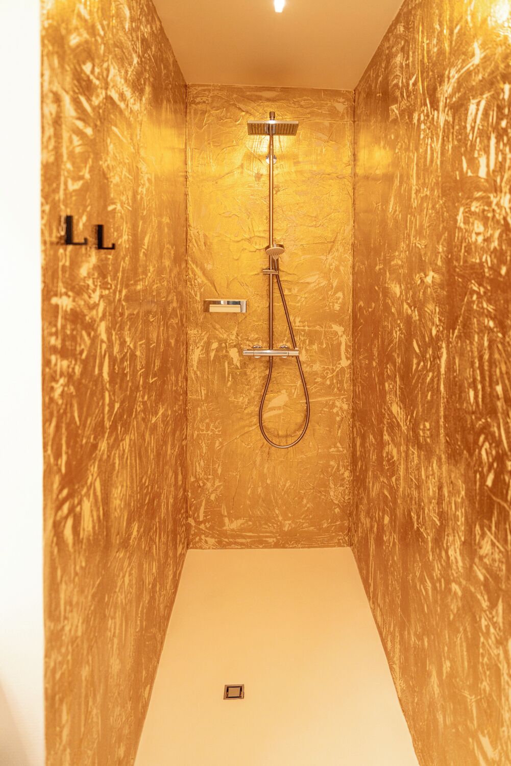 Un baño pequeño y cerrado con pared texturizada dorada, un cabezal de ducha y un panel de control.