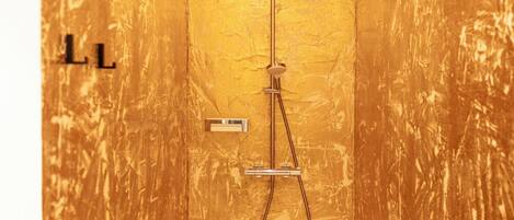 Un baño pequeño y cerrado con pared texturizada dorada, un cabezal de ducha y un panel de control.