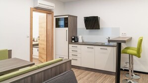 A compact kitchen with a built-in microwave, a coffee machine, and a small sink. There is a wooden door leading to another room, and a green chair is visible. - CHRIZZ Rooms (Graz)