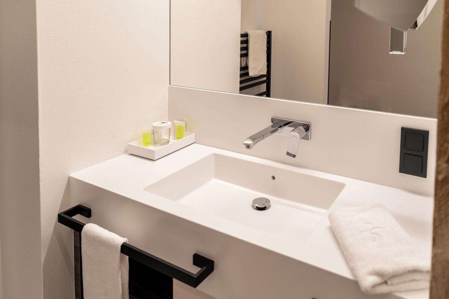 Un baño moderno con lavamanos blanco, un espejo y un perchero para toallas.