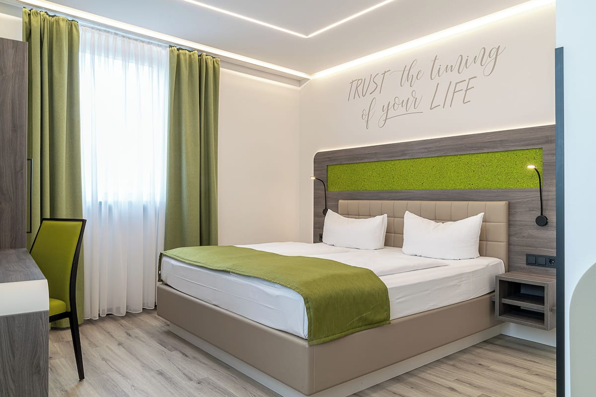 Ein modernes Hotelzimmer mit einem Bett, einem Schreibtisch und einem grünen Stuhl.