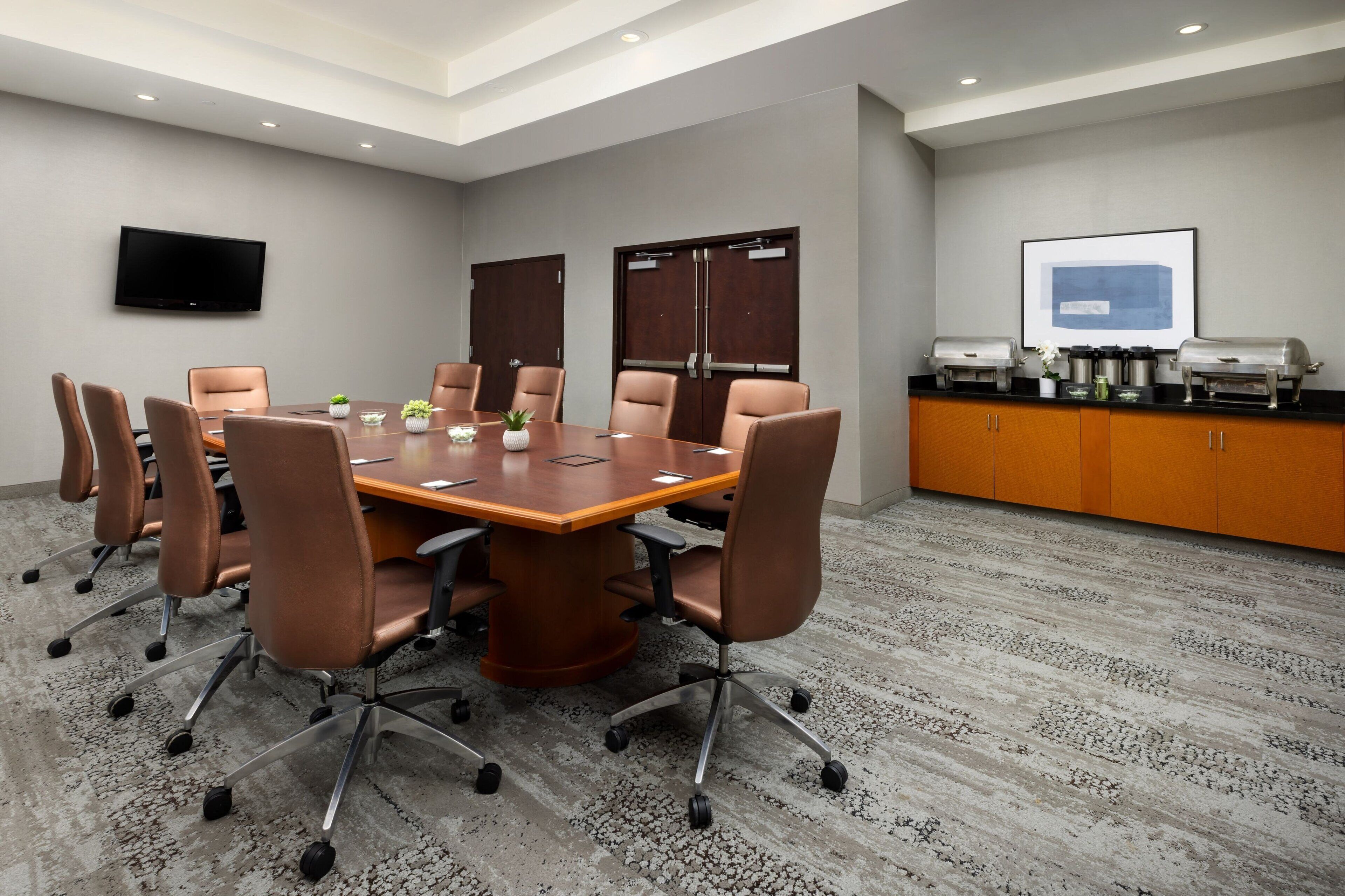 A conference room with a large table, chairs, a TV, and a coffee station.