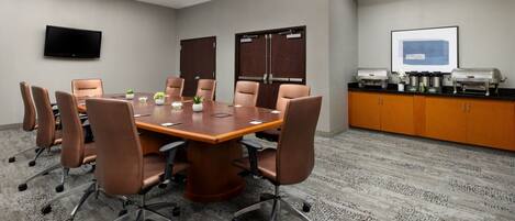 A conference room with a large table, chairs, a TV, and a coffee station.