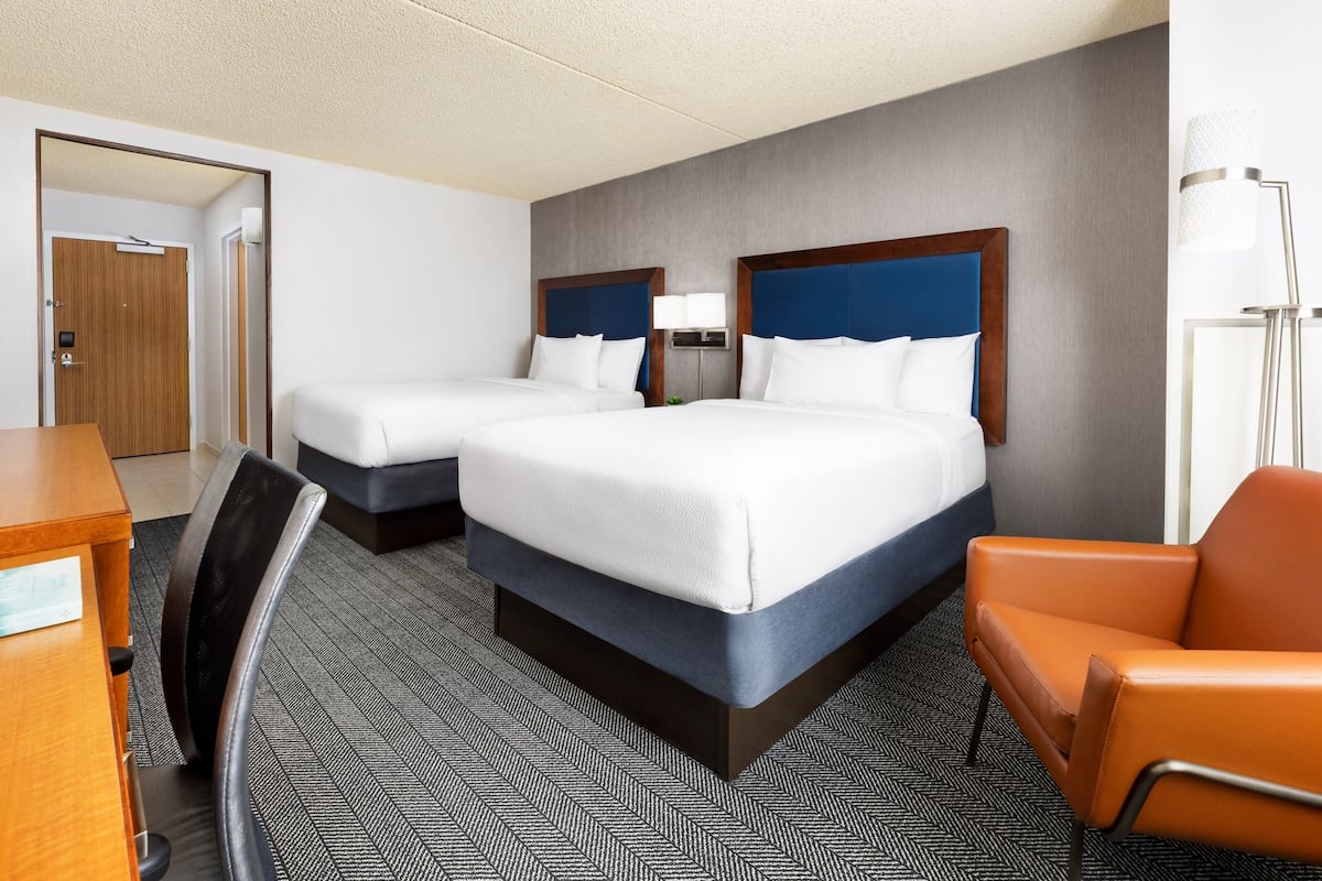 Ein Hotelzimmer mit zwei Betten, einem Schreibtisch, einem Stuhl und einer Lampe.