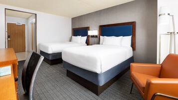 A hotel room with two beds, a desk, a chair, and a lamp.