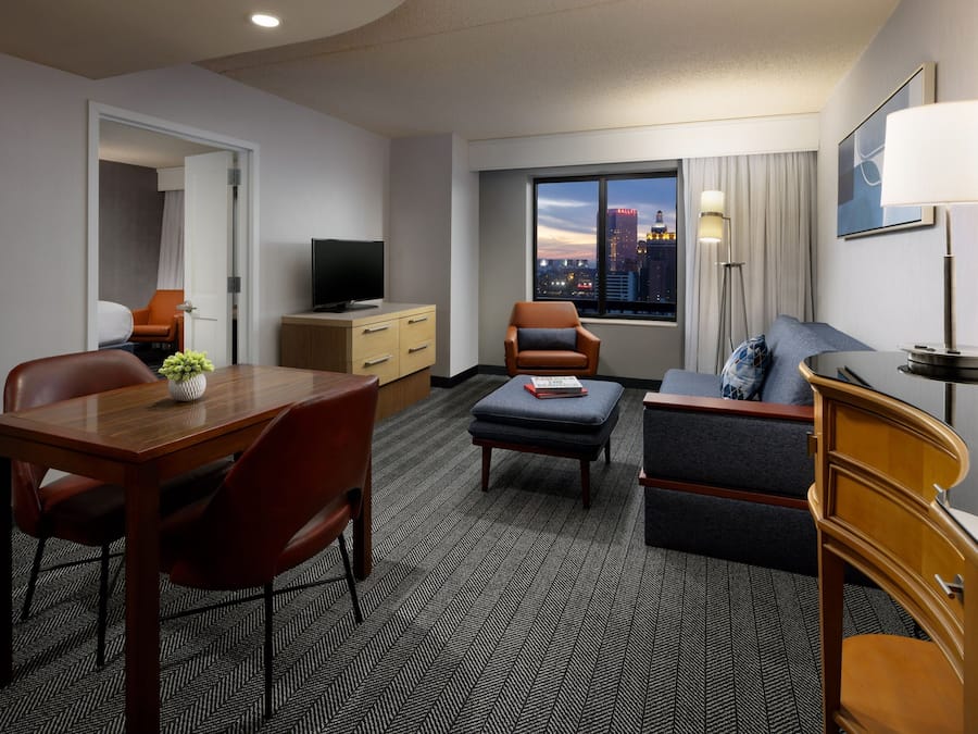 A hotel room with a dining area, a sofa, a TV, and a window with a city view.
