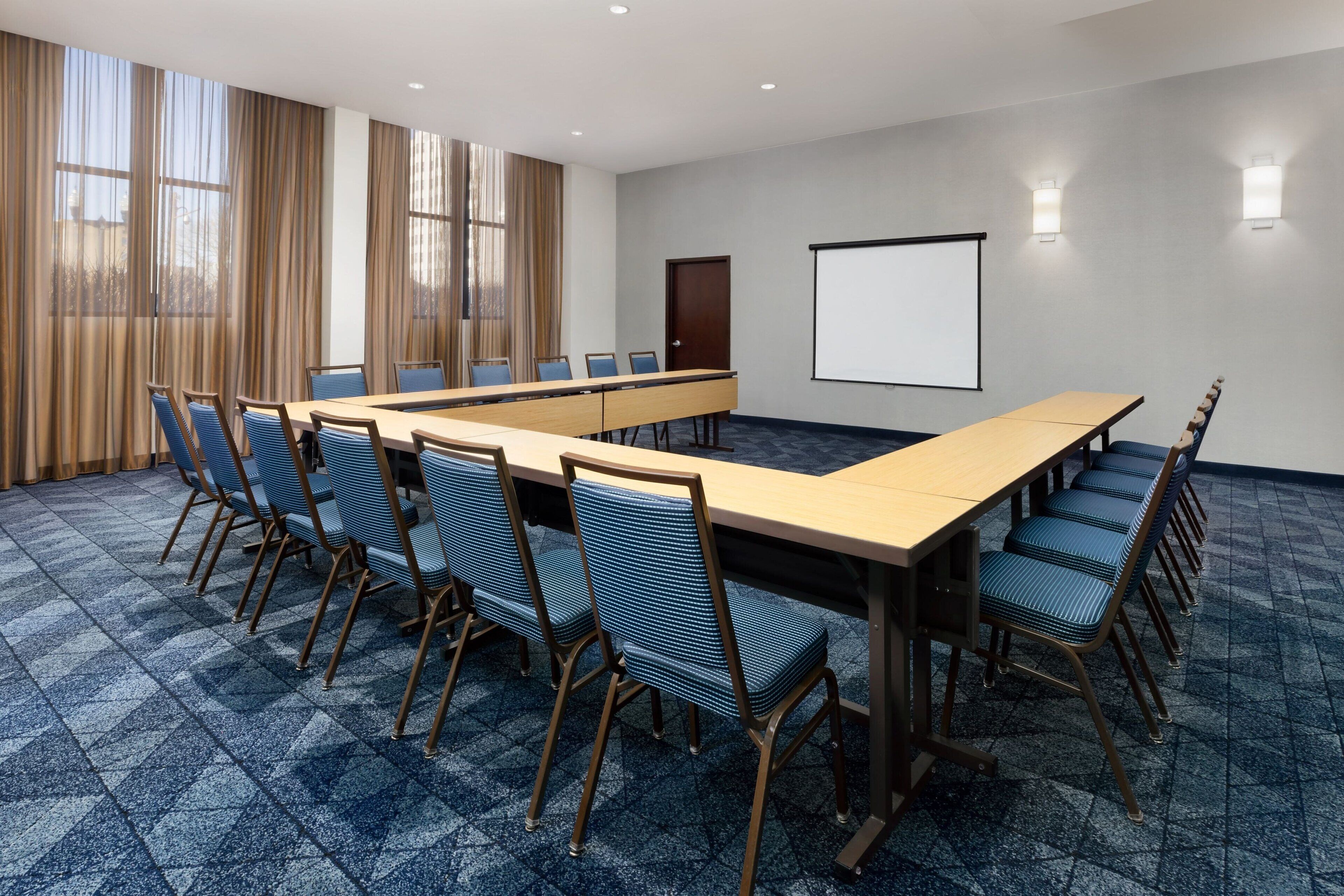 A conference room with a long table, blue chairs, a projector screen, and a door.