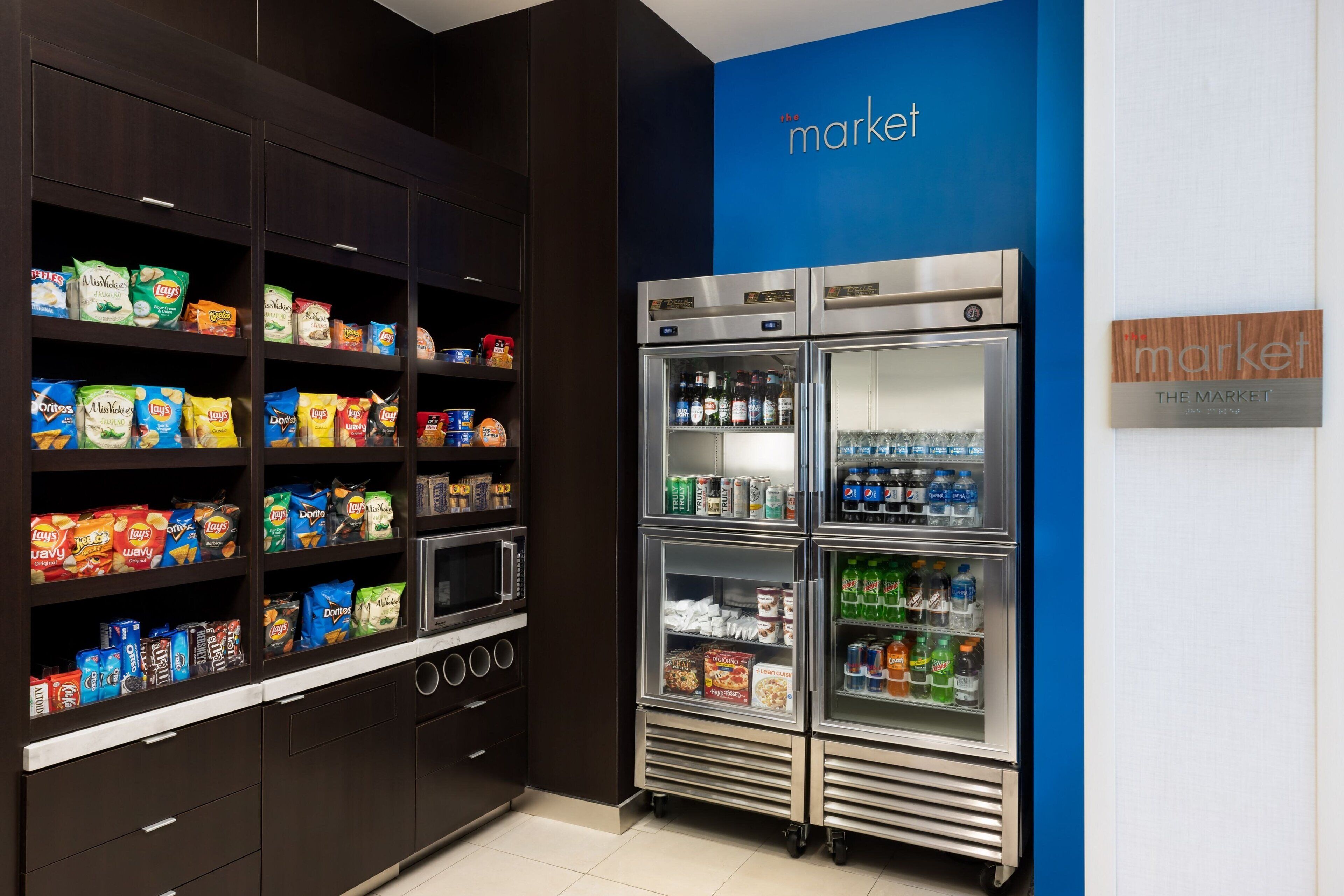 Un espace dédié aux collations et aux boissons, avec des étagères remplies de chips et un présentoir réfrigéré pour les boissons.