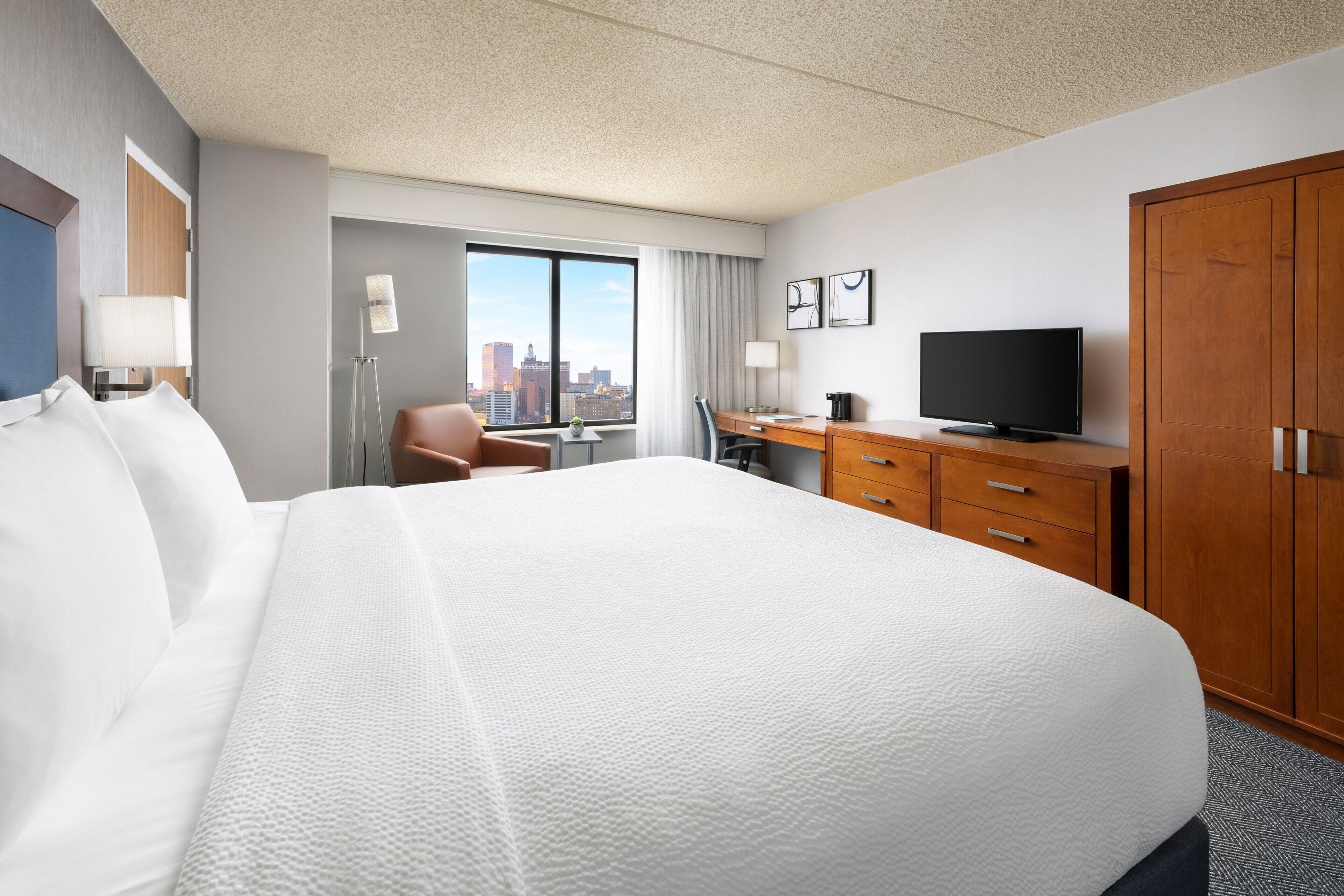 Een hotelkamer met een groot bed, een bureau met stoel, een televisie en een kledingkast.
