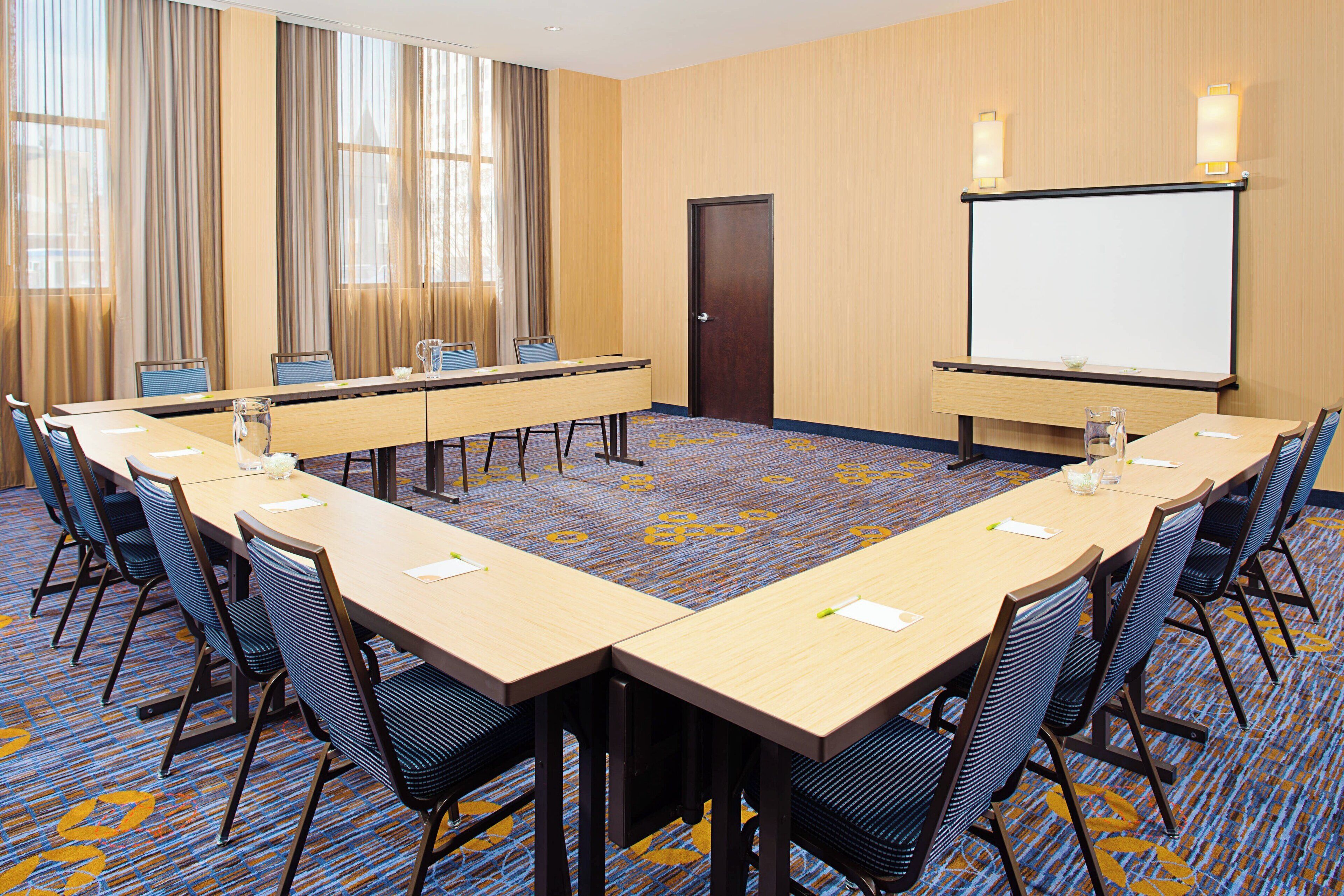 A conference room with a long table, chairs, a projector screen, and a door.