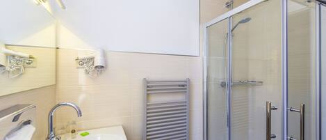 A modern bathroom with a sink, mirror, towel rack, and glass-enclosed shower.