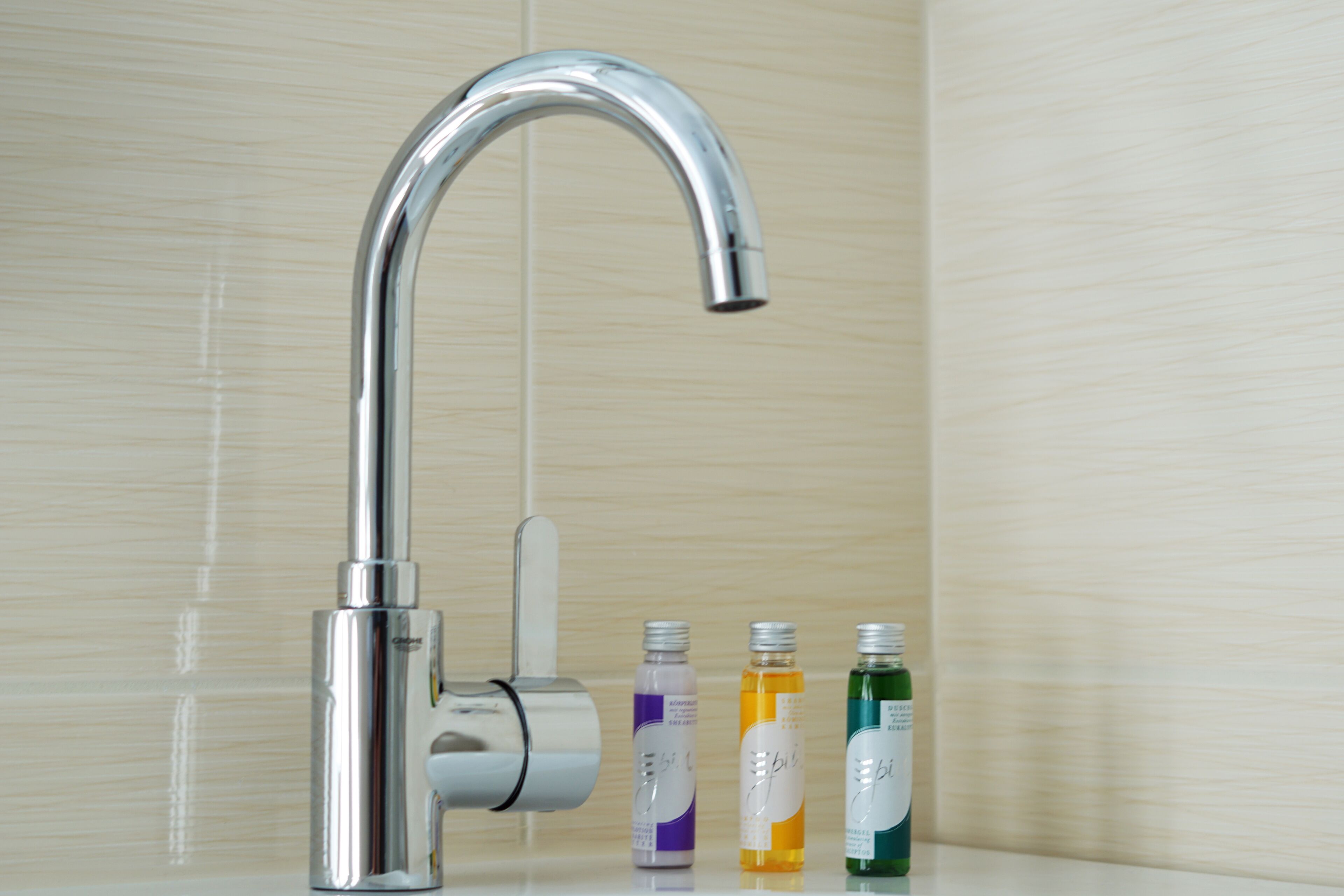 Un baño moderno con un grifo cromado, un perchero y tres botellas de jabón líquido.