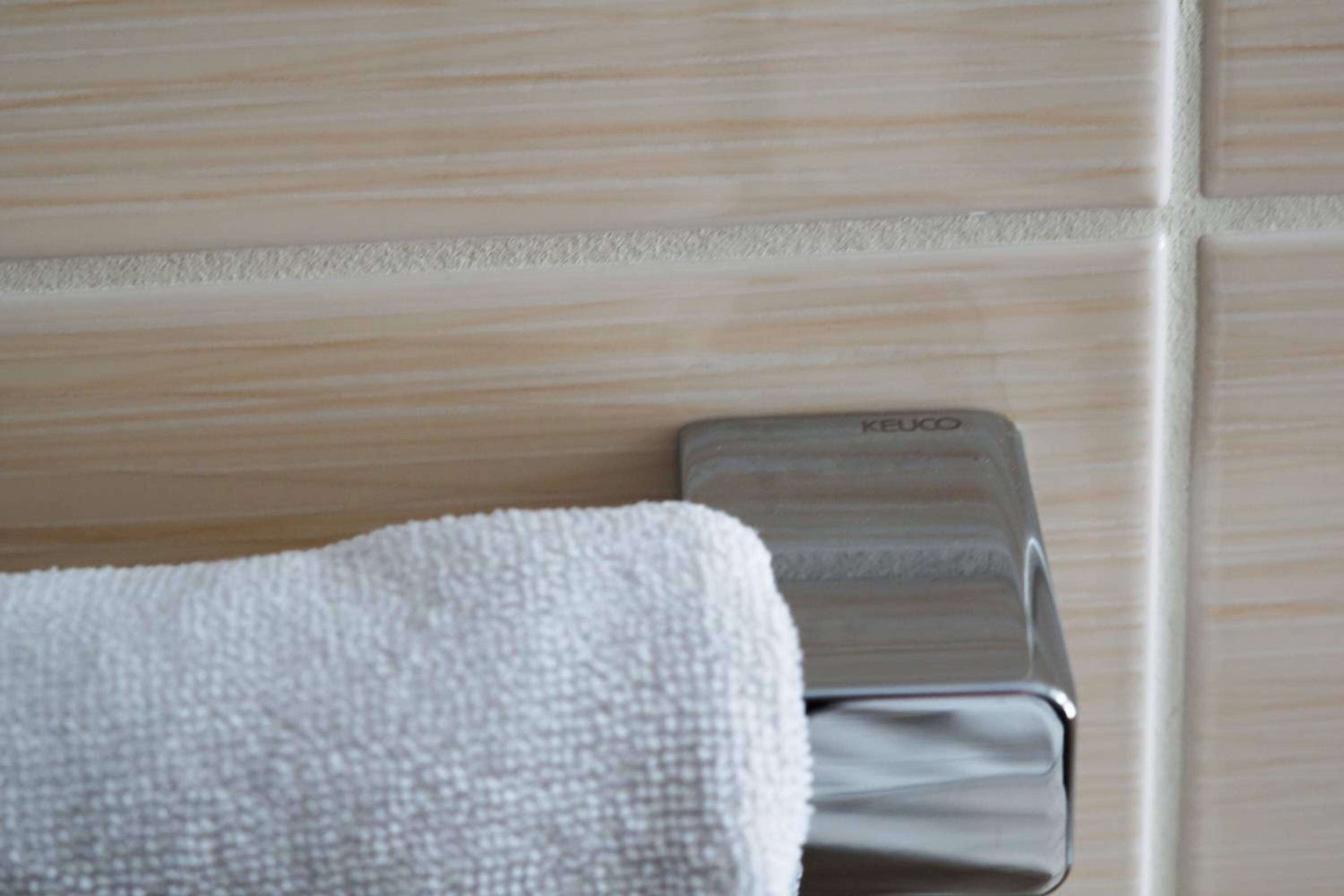 A bathroom with a towel hanging on a towel rack and a Keuco brand soap dispenser.