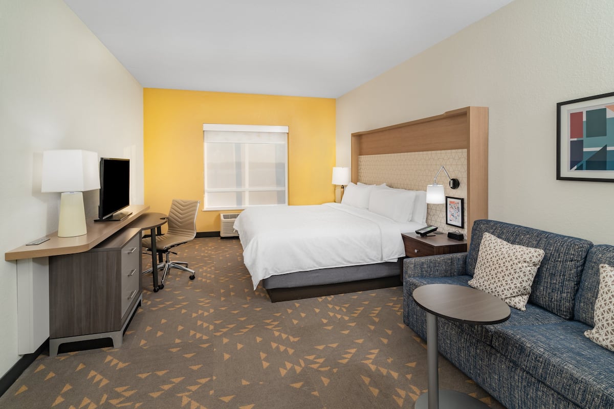A hotel room with a bed, a desk with a computer, a chair, a sofa, and a small table.
