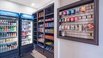 Una tienda con dispensadores de bebidas refrigeradas, estantes llenos de aperitivos y una pared exhibidora con bolsas colgantes.
