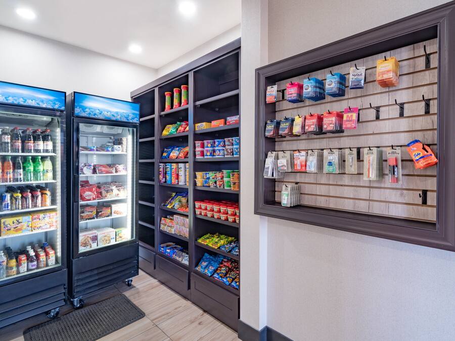 Una tienda con dispensadores de bebidas refrigeradas, estantes llenos de aperitivos y una pared exhibidora con bolsas colgantes.