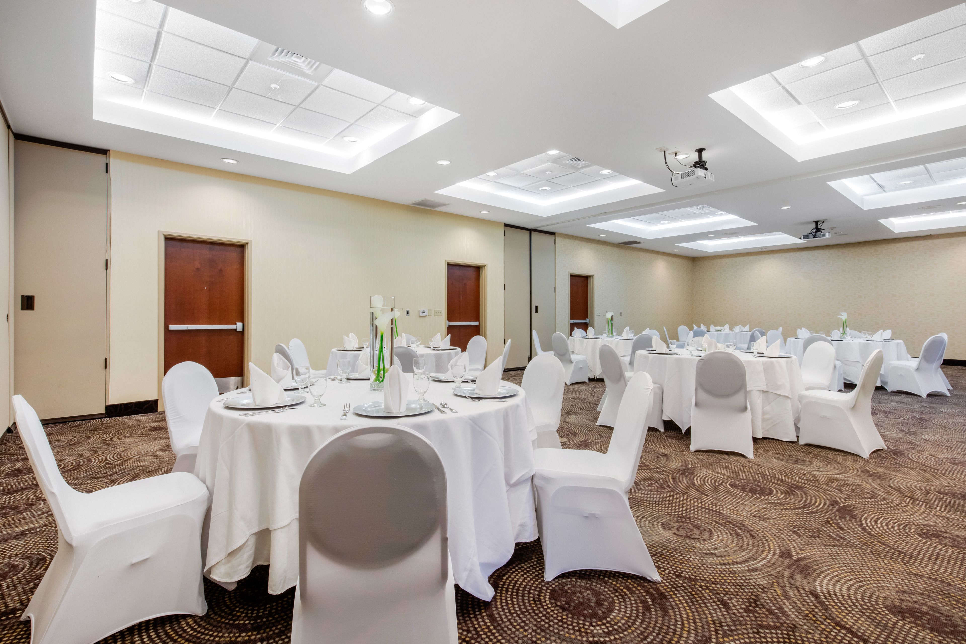 Un salón de conferencias con mesas redondas, sillas blancas e iluminación en el techo.