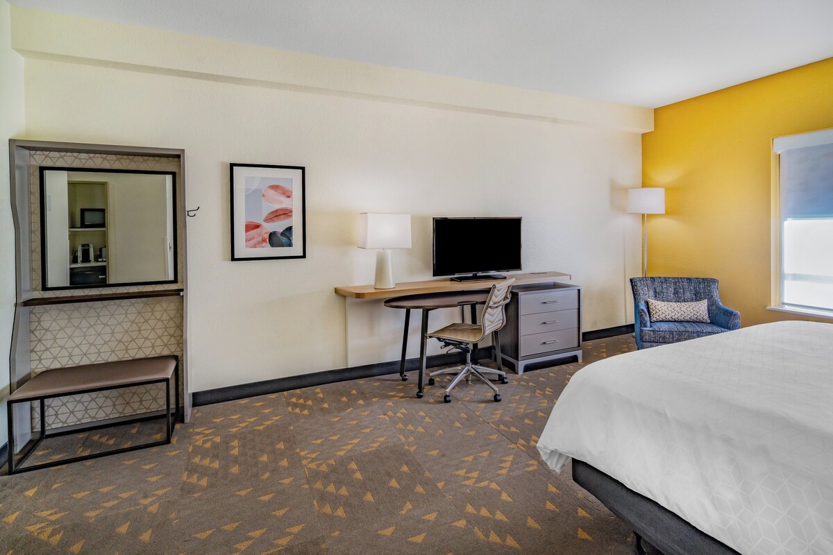 A hotel room with a bed, desk, chair, TV, and a small bench.