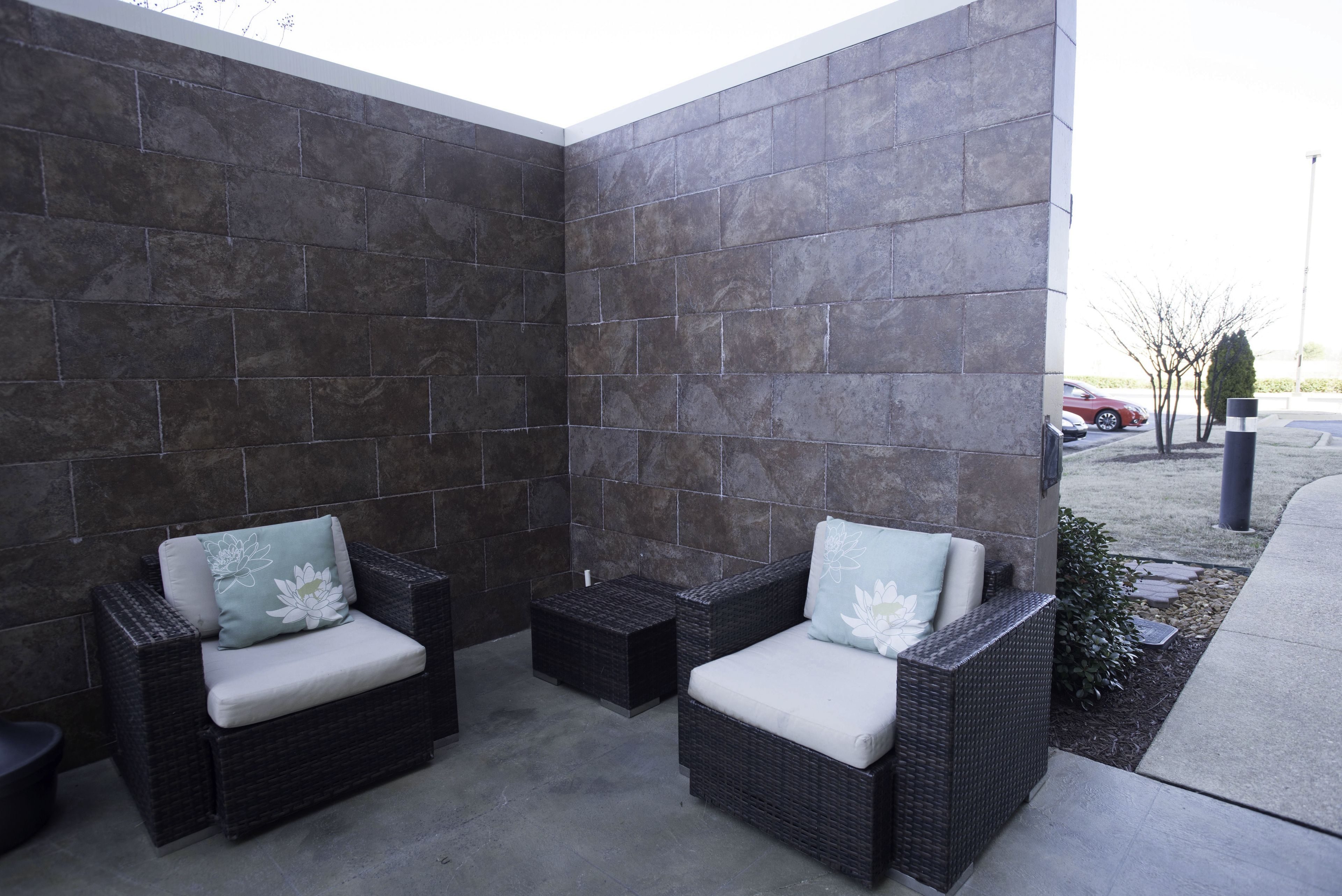 Un patio con dos sofás de mimbre y una pequeña mesa, frente a un muro de piedra.
