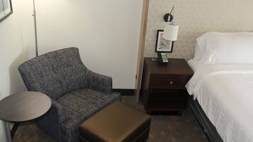 A hotel room with a single bed, a small round table, a chair, a nightstand with a lamp, and a map on the wall.