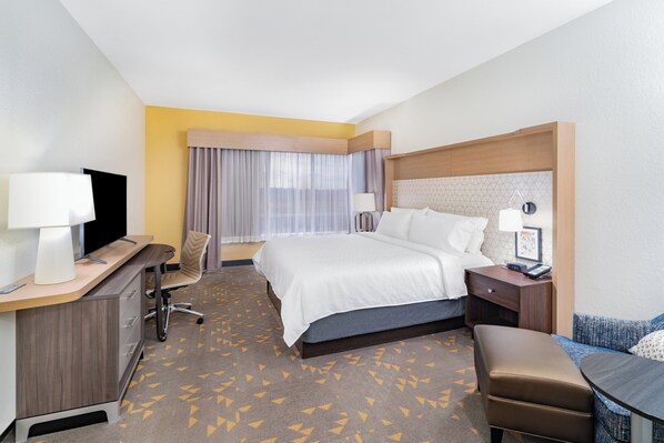 A hotel room with a bed, desk, chair, bedside table, lamp, and a television. - Holiday Inn Southaven Central - Memphis by IHG (Southaven)