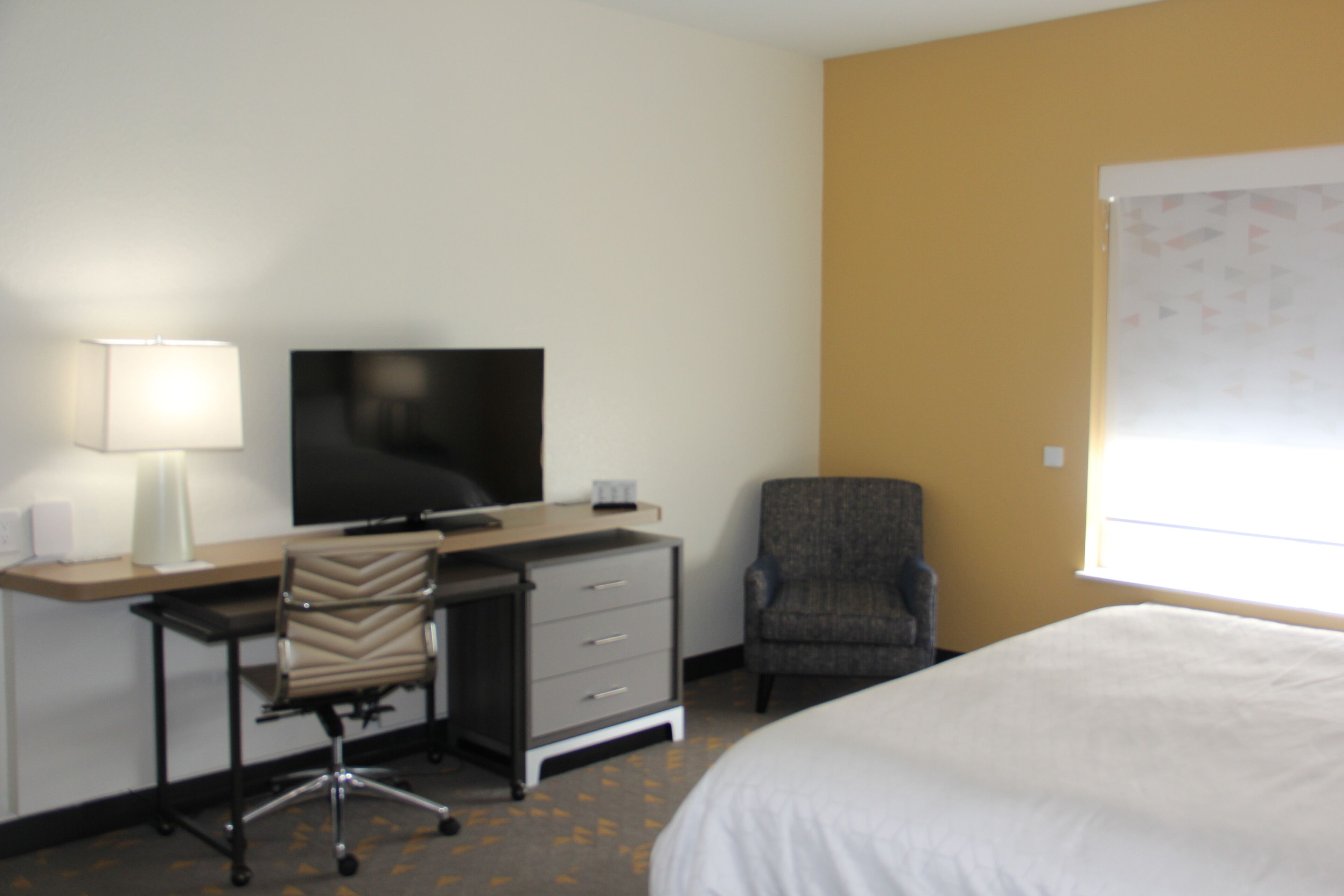 A hotel room with a bed, a desk with a chair, a television, and a window.