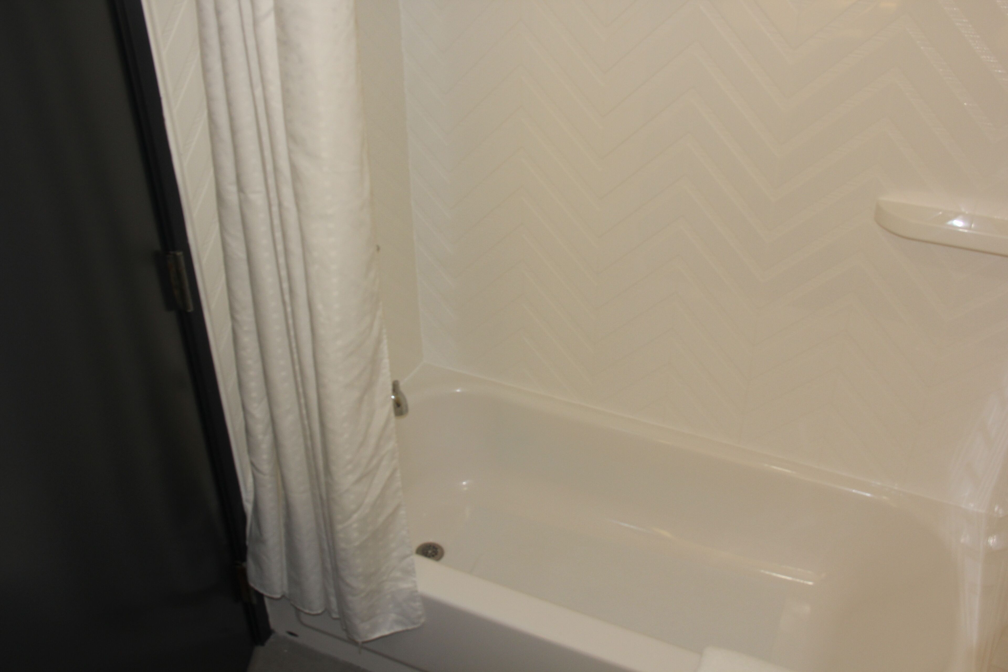 Une salle de bain avec une baignoire, un rideau de douche et un mur recouvert de carreaux blancs.