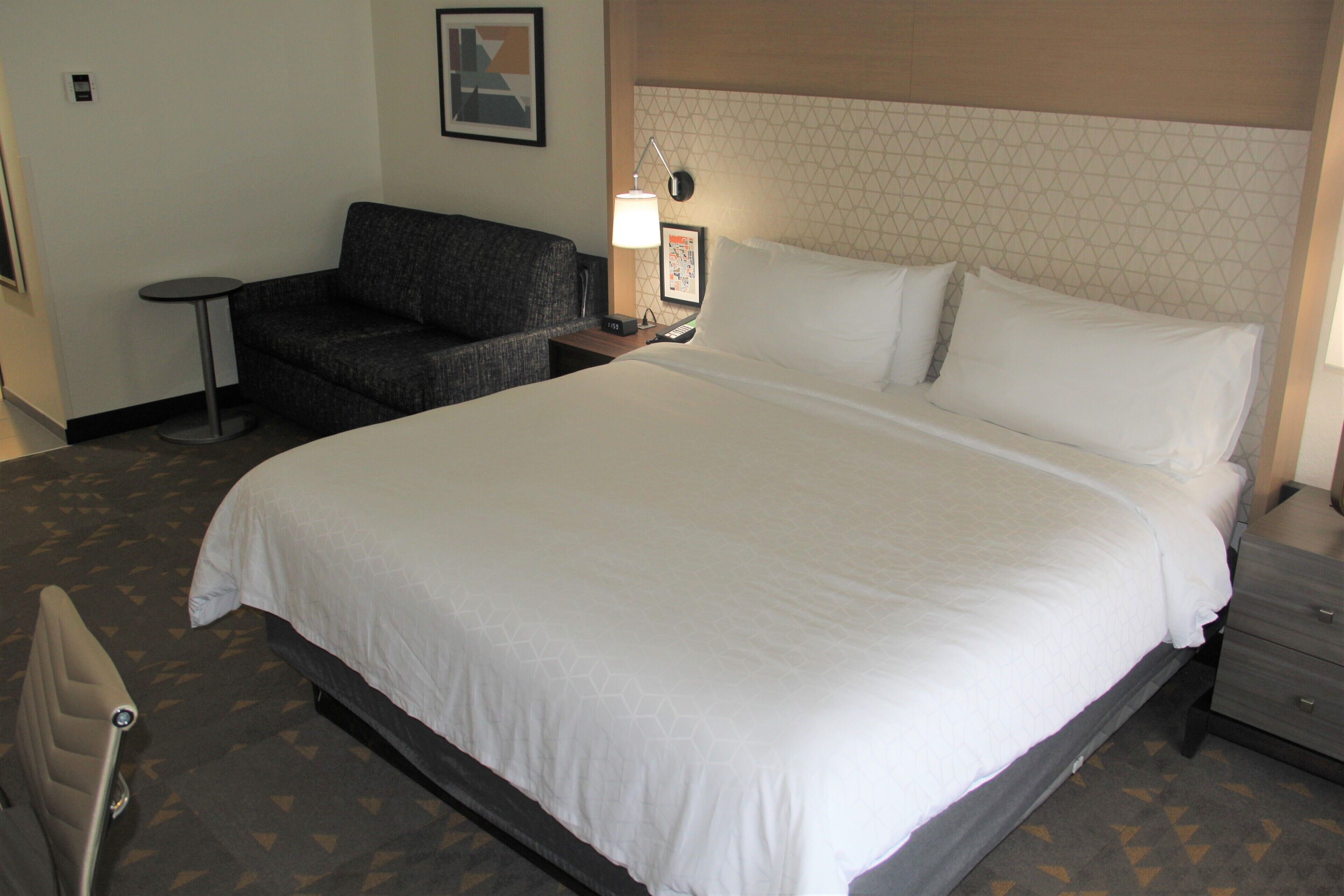 A hotel room with a large bed, a small sofa, a bedside table with a lamp, and a framed picture on the wall.