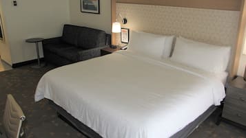 A hotel room with a large bed, a small sofa, a bedside table with a lamp, and a framed picture on the wall.