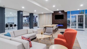 A modern hotel lobby with a sofa, armchairs, a dining table, and a TV mounted on the wall. - Holiday Inn Southaven Central - Memphis by IHG (Southaven)
