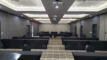 Un salón de conferencias con filas de mesas y sillas, un proyector y una alfombra estampada.