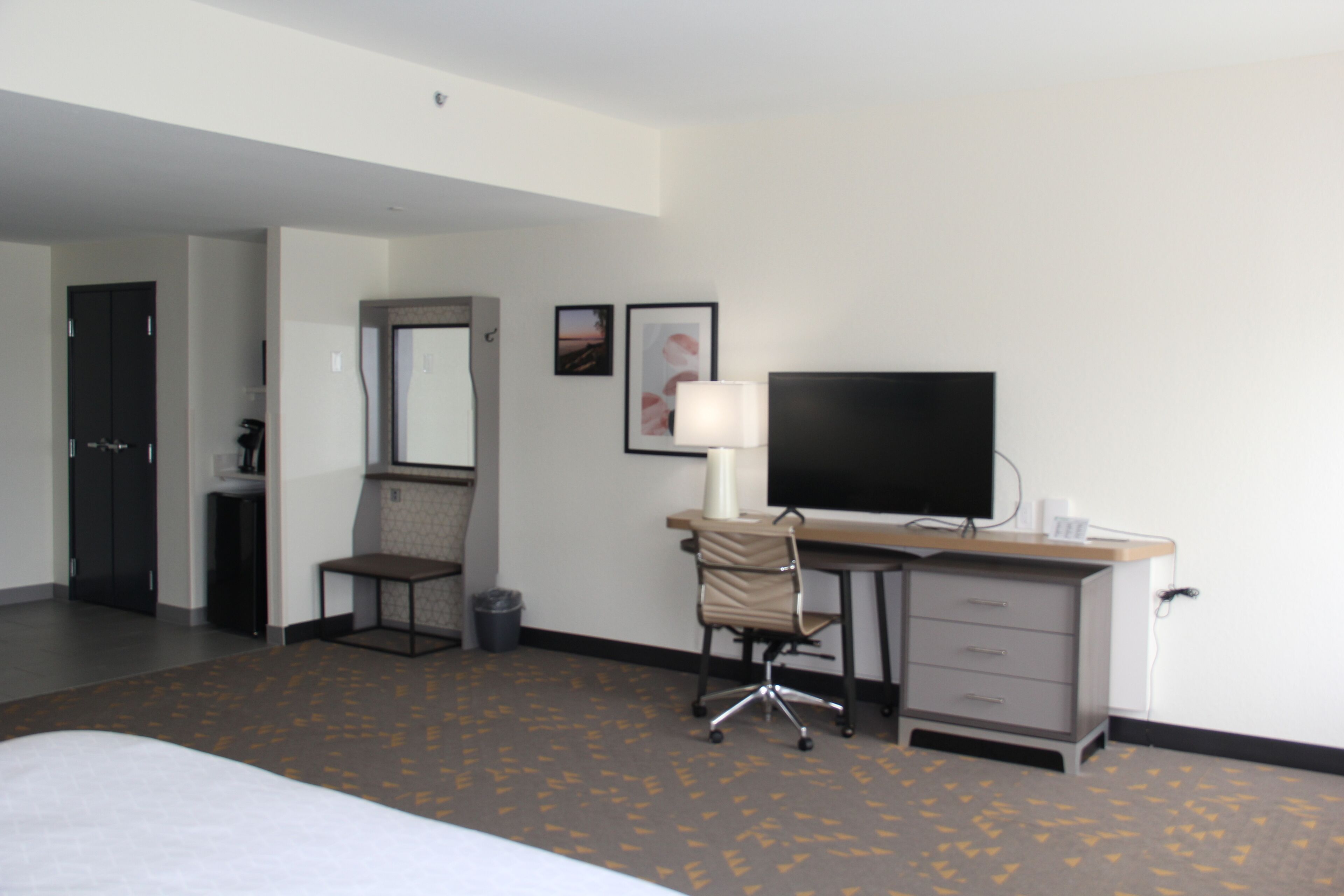A hotel room with a bed, a desk with a computer, a chair, a TV, a mirror, and a trash bin.