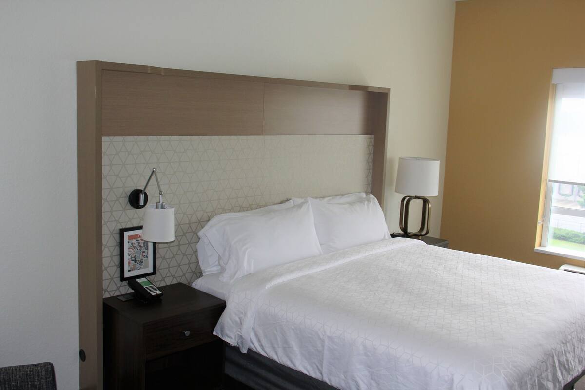 A neatly made bed with white linens, a bedside table with a lamp, and a wall-mounted phone.