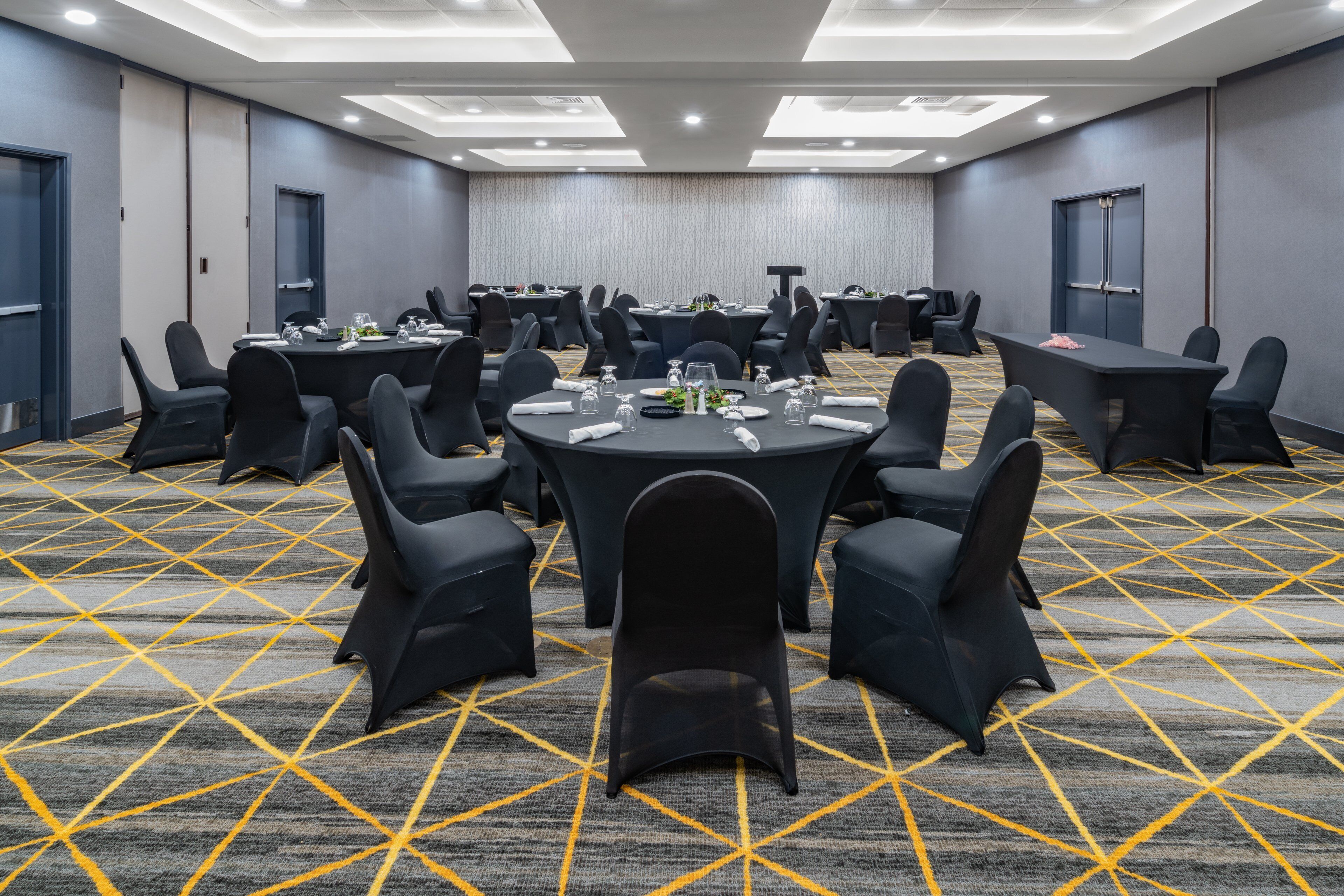 Un salón de conferencias con varias mesas y sillas, piso alfombrado y un diseño moderno en el techo.